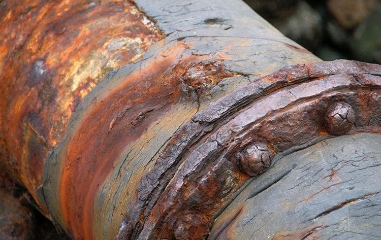 Exemple de fissuration par corrosion sous contrainte sur un conduit métallique dans une structure ancienne.