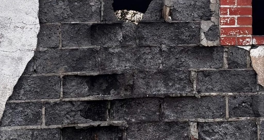 Zoom sur des moellons de mâchefer montrant une texture sombre et poreuse avec présence de fragments de charbon caractéristiques de ce matéri