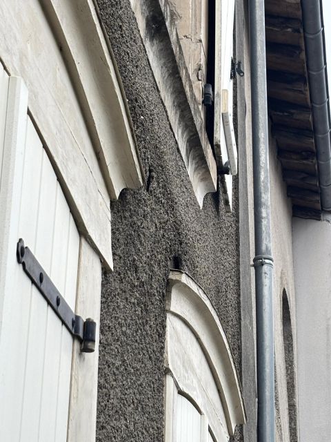 Vue rapprochée d’une façade enduite au ciment présentant un décollement de l’enduit autour d’une ouverture, avec fissures visibles et traces d’humidité au niveau des encadrements.