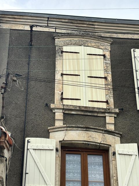 Façade d’un bâtiment ancien avec fissures marquées autour des encadrements de fenêtres et dégradations de l’enduit ciment, révélant des tensions dans la maçonnerie et des désordres structurels.