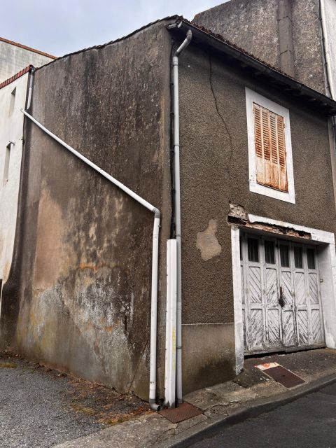 Angle de bâtiment montrant des traces d’humidité et de coulures sur le pignon, avec une descente d’eau pluviale et une fissure visible en façade côté rue.